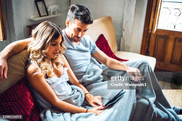 young couple cuddling on couch at home watching tablet - lovers 2020 film fotografías e imágenes de stock