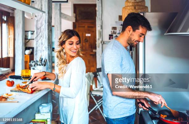 happy young couple preparing food together in kitchen at home - young couple cooking stock pictures, royalty-free photos & images