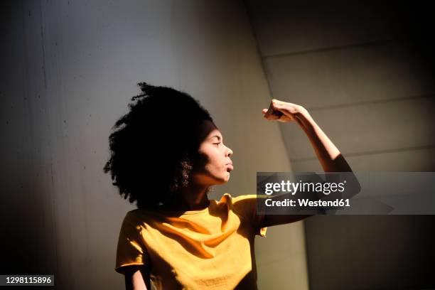 young woman showing muscles while standing against wall - equal opportunity stock-fotos und bilder