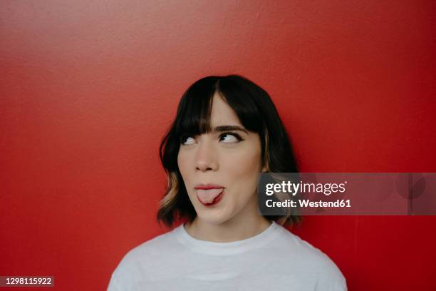 young woman sticking out tongue while looking up against red background - protruding ストックフォトと画像