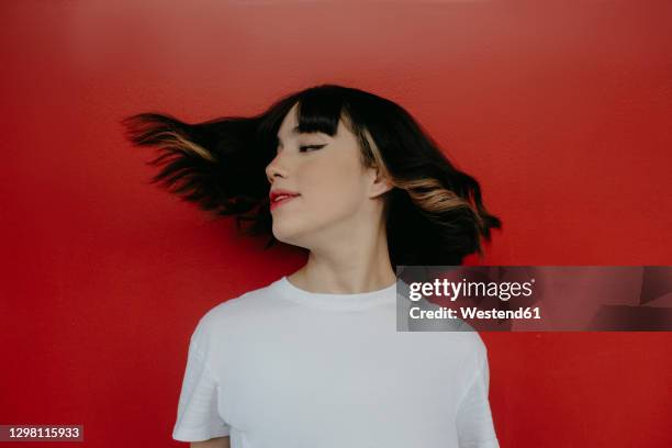 young woman tossing hair against red background - bangs stock-fotos und bilder