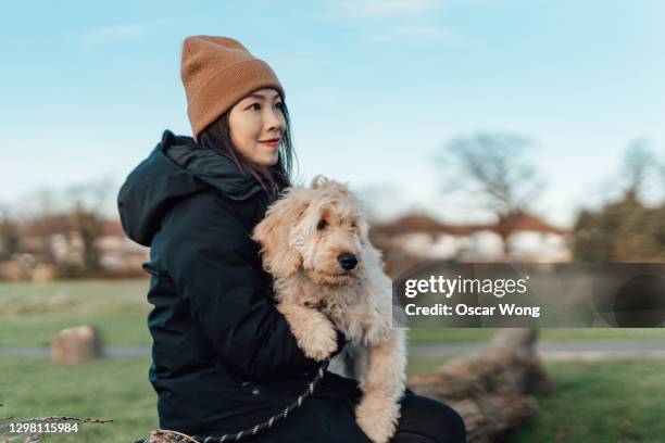 young woman relaxing at the park with her dog - cappotto invernale foto e immagini stock