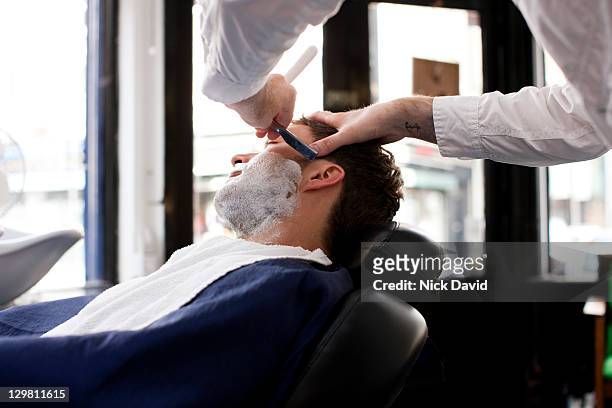 a young man getting a wet shave in a traditional barbers shop - barberare bildbanksfoton och bilder