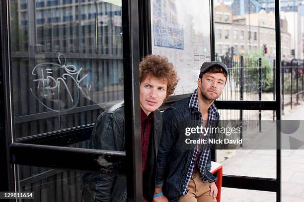 two young men waiting for a bus at a london bus stop - bus stop uk stock pictures, royalty-free photos & images