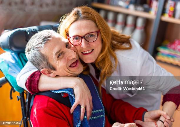 smiling female healthcare worker embracing disabled man at rehabilitation center - promises rehab center bildbanksfoton och bilder