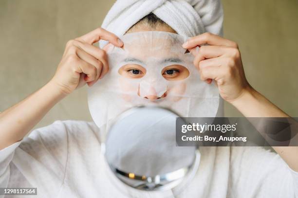 portrait of young woman looking her face in mirror before applying facial mask for enhance her skin. - masker stockfoto's en -beelden