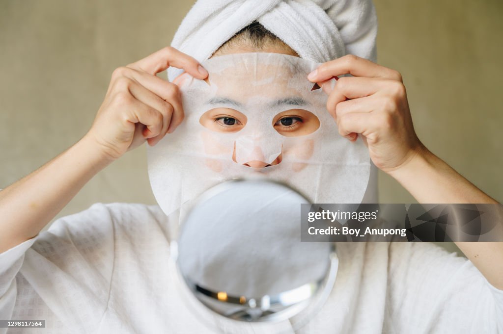 Portrait of young woman looking her face in mirror before applying facial mask for enhance her skin.