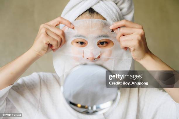 portrait of young woman looking her face in mirror before applying facial mask for enhance her skin. - beauty mask stock pictures, royalty-free photos & images