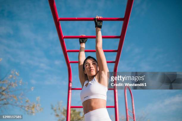 confident sportswoman hanging on monkey bars while sports training in public park - cage à poules photos et images de collection