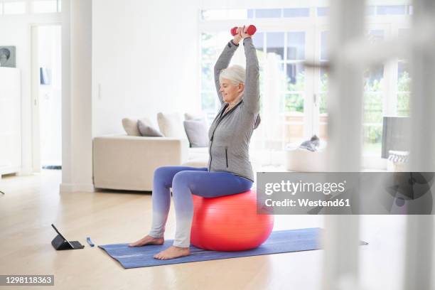 retired woman exercising while learning from online tutorial through digital tablet at home - pilates ball man stock-fotos und bilder
