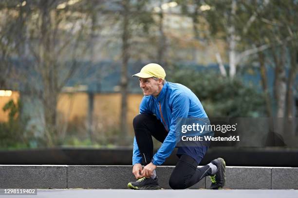 smiling mature man tying shoelace on footpath while exercising - stringa foto e immagini stock