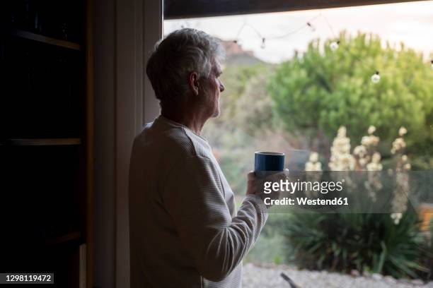 man drinking coffee while standing by window at home - ausblick stock-fotos und bilder