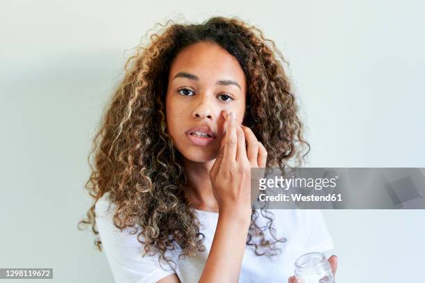 young woman applying facial cream against white wall - concealer stock pictures, royalty-free photos & images