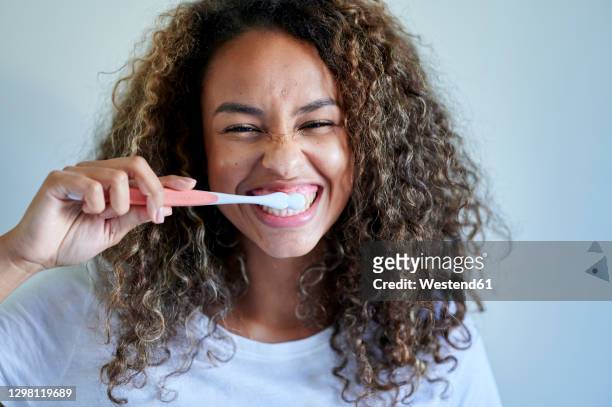 cheerful young woman enjoying while brushing teeth against wall - toothbrush photos et images de collection