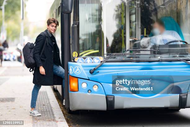 smiling handsome young man with backpack boarding bus in city - boarding a bus stock-fotos und bilder