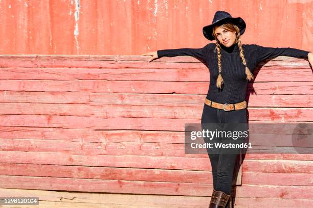 portrait of female rancher leaning against fence - cowgirl hairstyles fotografías e imágenes de stock