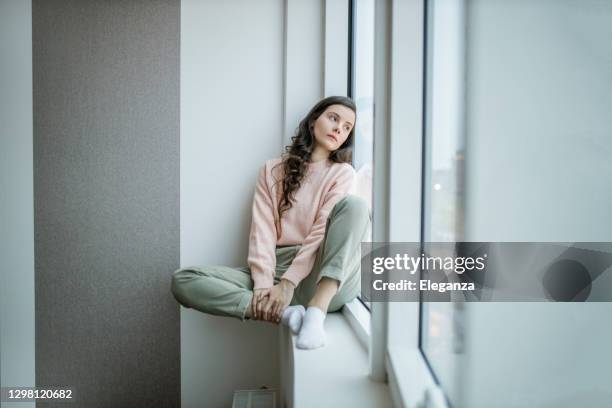 depressed woman at home feeling sad. woman looks sadly outside the window. depressed lonely lady standing alone and looking through the window. - reclusão imagens e fotografias de stock