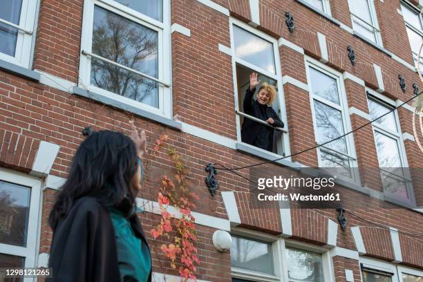 young woman waving through window to female friend standing outside - sventolare la mano foto e immagini stock