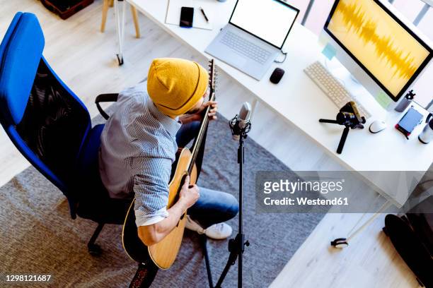 male vlogger playing guitar while live streaming on camera at recording studio - live broadcast stock-fotos und bilder