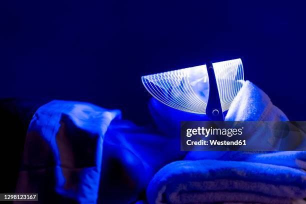 young woman wearing blue mask during rejuvenating treatment in dark at beauty spa - luminothérapie photos et images de collection