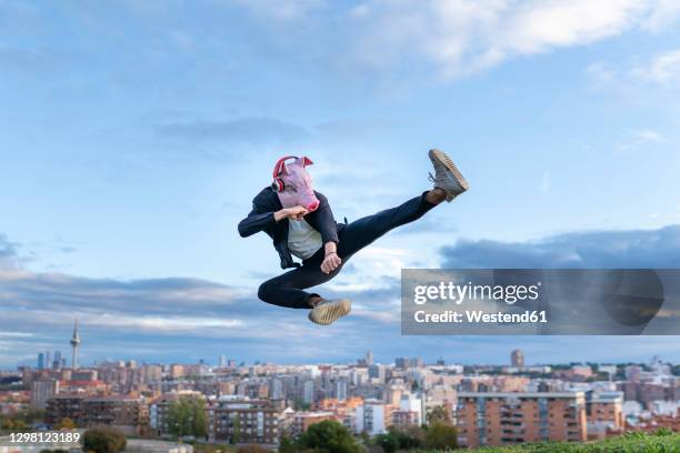 male professional wearing pig mask practicing kickboxing while jumping against sky - face guard sport stock-fotos und bilder