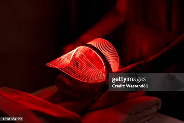 young woman wearing red mask during rejuvenating treatment at beauty spa - kosmetikmaske stock-fotos und bilder