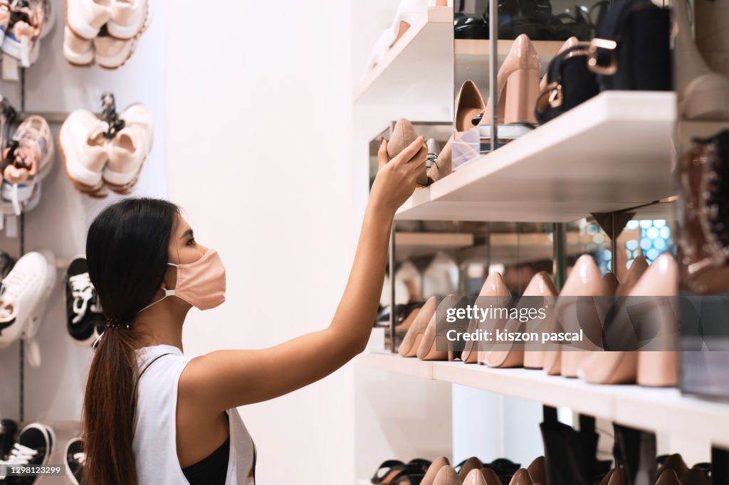 Young Asian woman wearing face mask in the boutique . She's choosing shoes in store