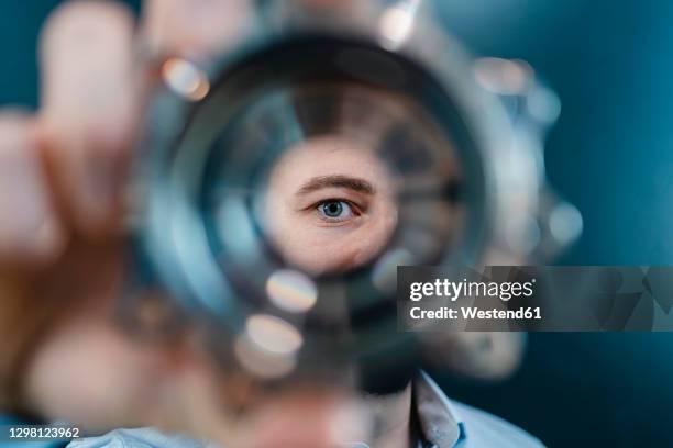 male professional's eyes seen through circular machine part in factory - industrie und mensch stock-fotos und bilder