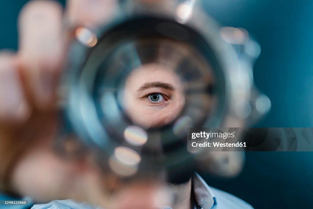 Male professional's eyes seen through circular machine part in factory