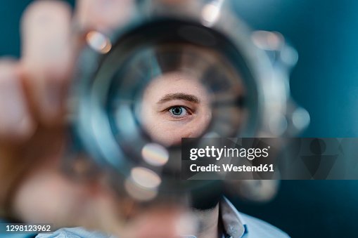 Male professional's eyes seen through circular machine part in factory Male professional's eyes seen through circular machine part in factory