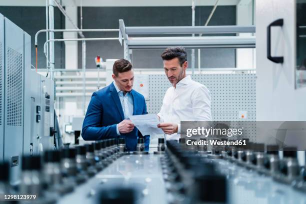 male professionals discussing over document while standing by manufacturing equipment in factory - papierwerk stock-fotos und bilder