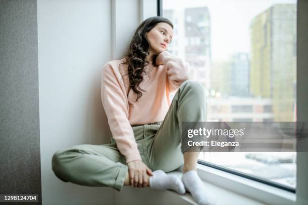 depressed woman at home feeling sad. woman looks sadly outside the window. depressed lonely lady standing alone and looking through the window. - fobia imagens e fotografias de stock