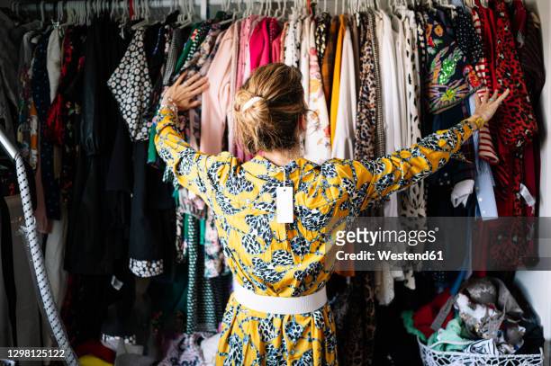 fashionable blond woman in new yellow dress choosing from clothes rack at apartment - clothes wardrobe stockfoto's en -beelden