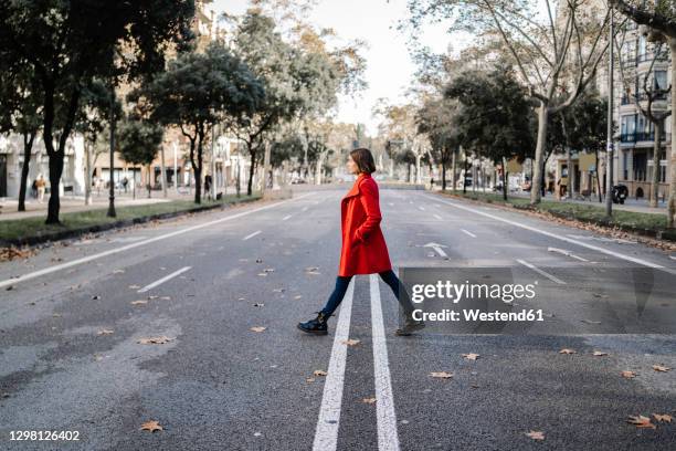 fashionable woman wearing winter jacket walking on road - red coat foto e immagini stock
