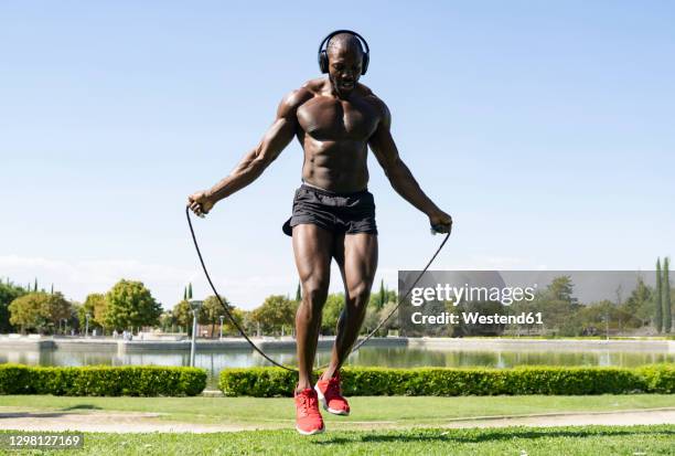 sportsman doing skipping exercise while listening music through headphones in park on sunny day - jump rope stock pictures, royalty-free photos & images