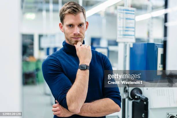 confident businessman with hand on chin standing in factory - hand am kinn stock-fotos und bilder