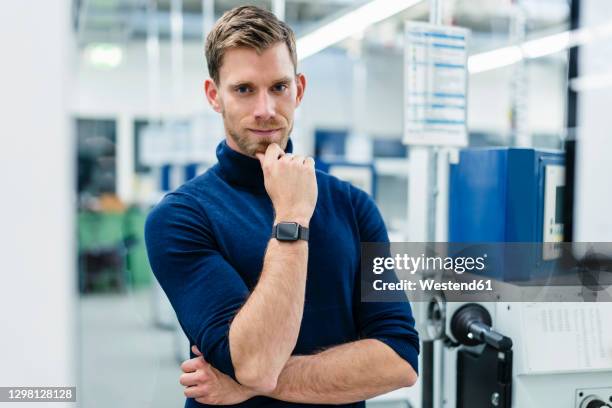 confident businessman with hand on chin standing in factory - man hand on chin stock pictures, royalty-free photos & images