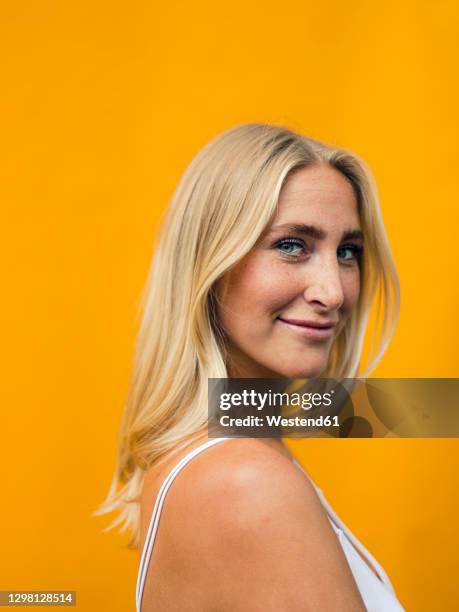 young woman smiling by yellow wall - blond hair young woman sunshine stockfoto's en -beelden