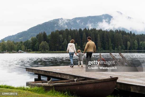 family with little daughter walking together on lakeshore jetty - three people walking stock pictures, royalty-free photos & images