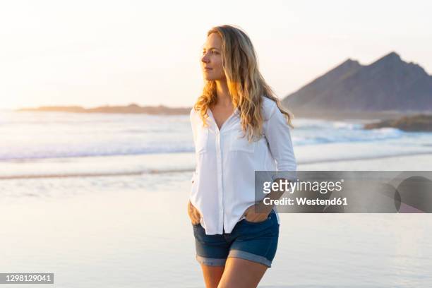 beautiful woman with hands in pockets looking away while walking at beach - short hair photos et images de collection