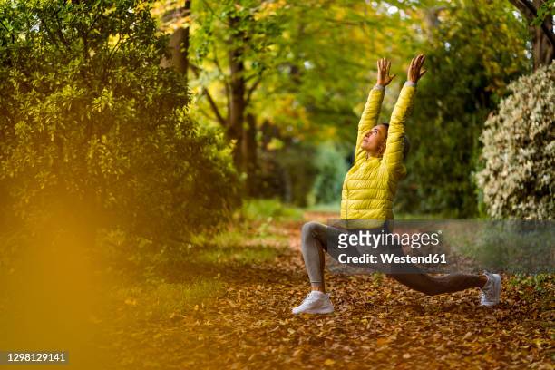 athlete with hand raised doing yoga while exercising on footpath at park - beleza e cuidados com o corpo - fotografias e filmes do acervo