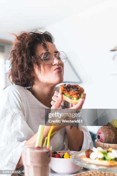 portrait of young woman wearing eyeglasses and nose ring eating breakfast - sandwich stock-fotos und bilder