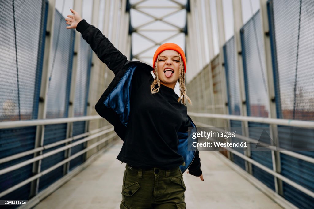 Happy young woman with eyes closed sticking out tongue while dancing on footbridge