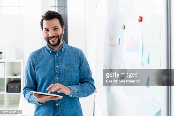 portrait of smiling business man standing at whiteboard in office - denim shirt stock pictures, royalty-free photos & images