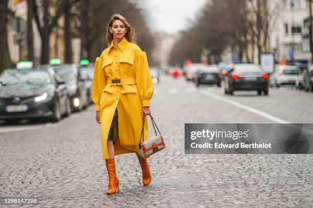 Natalia Verza aka Mascarada wears earrings, a bold yellow long trench coat from Fendi, a Fendi black and white checked Fendi bag with brown leather...
