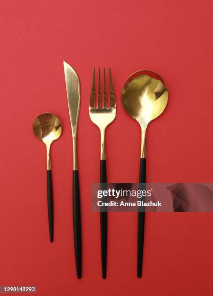 close-up of black and golden cutleries over red background - butter knife stock pictures, royalty-free photos & images