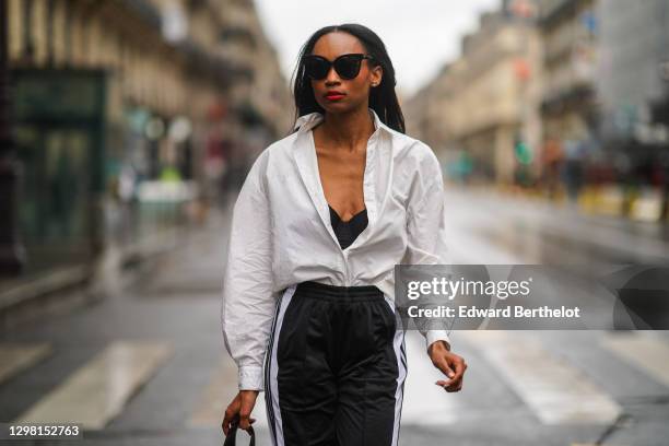 Emilie Joseph wears sunglasses, a white oversized long shirt from & Other Stories, black bras from Aubade, a Danse Lente black leather bag, black and...