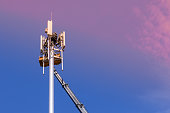 Workers install cellular base station with transmitters 3G, 4G, 5G and antennas on cell tower on background of pink-blue sky. Mobile telecommunication equipments. Copy space