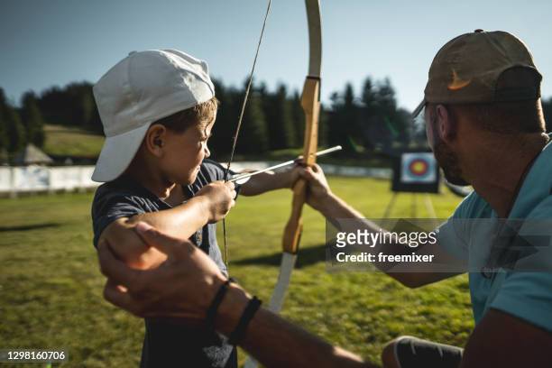 little boy learning how to use bow with instructor - bow arrow stock pictures, royalty-free photos & images