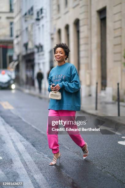 Ellie Delphine aka SlipIntoStyle wears earrings, a blue oversized wool pullover from Rotate, neon pink jogger sport pants from Rotate, a small white...